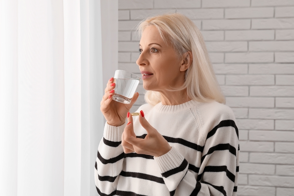 Mature,Woman,Taking,Fish,Oil,Pill,Near,White,Brick,Wall